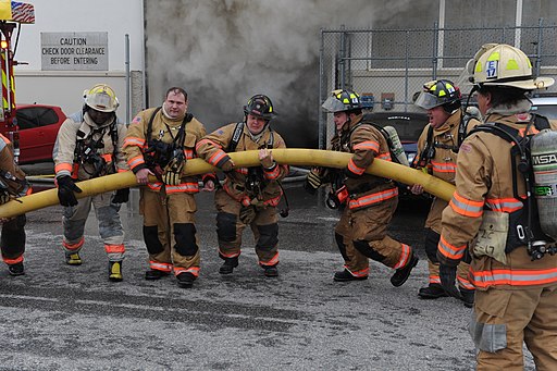 Firefighters carrying a water hose to extinguish a warehouse fire