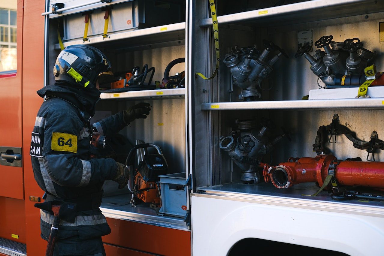 A firefighter stands ready with fire engine equipment at the ready.